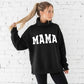 Woman wearing a black hoodie with 'MAMA' printed on it against a white brick wall.
