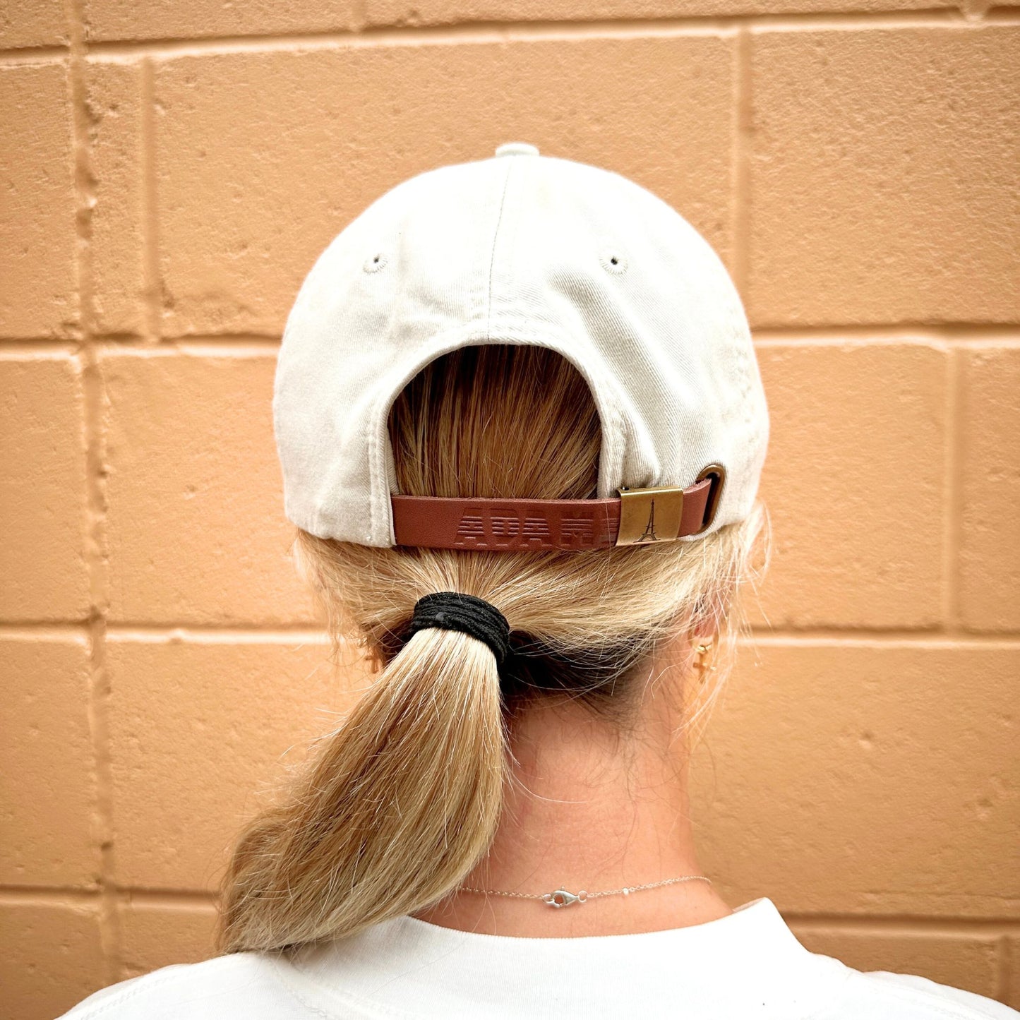 Back image of a person wearing a white cap with a brown strap 