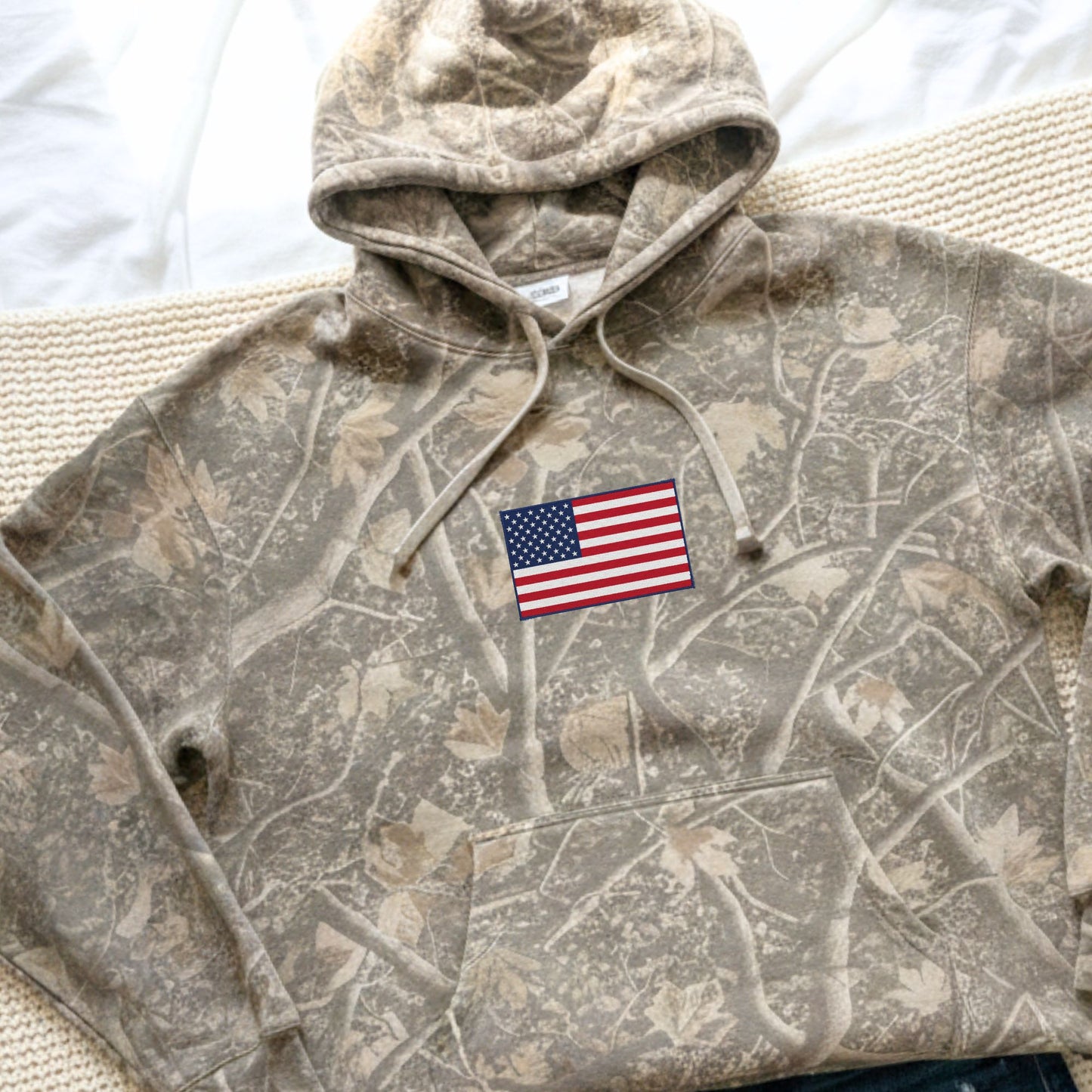 Camouflage hoodie with an American flag patch on a neutral background