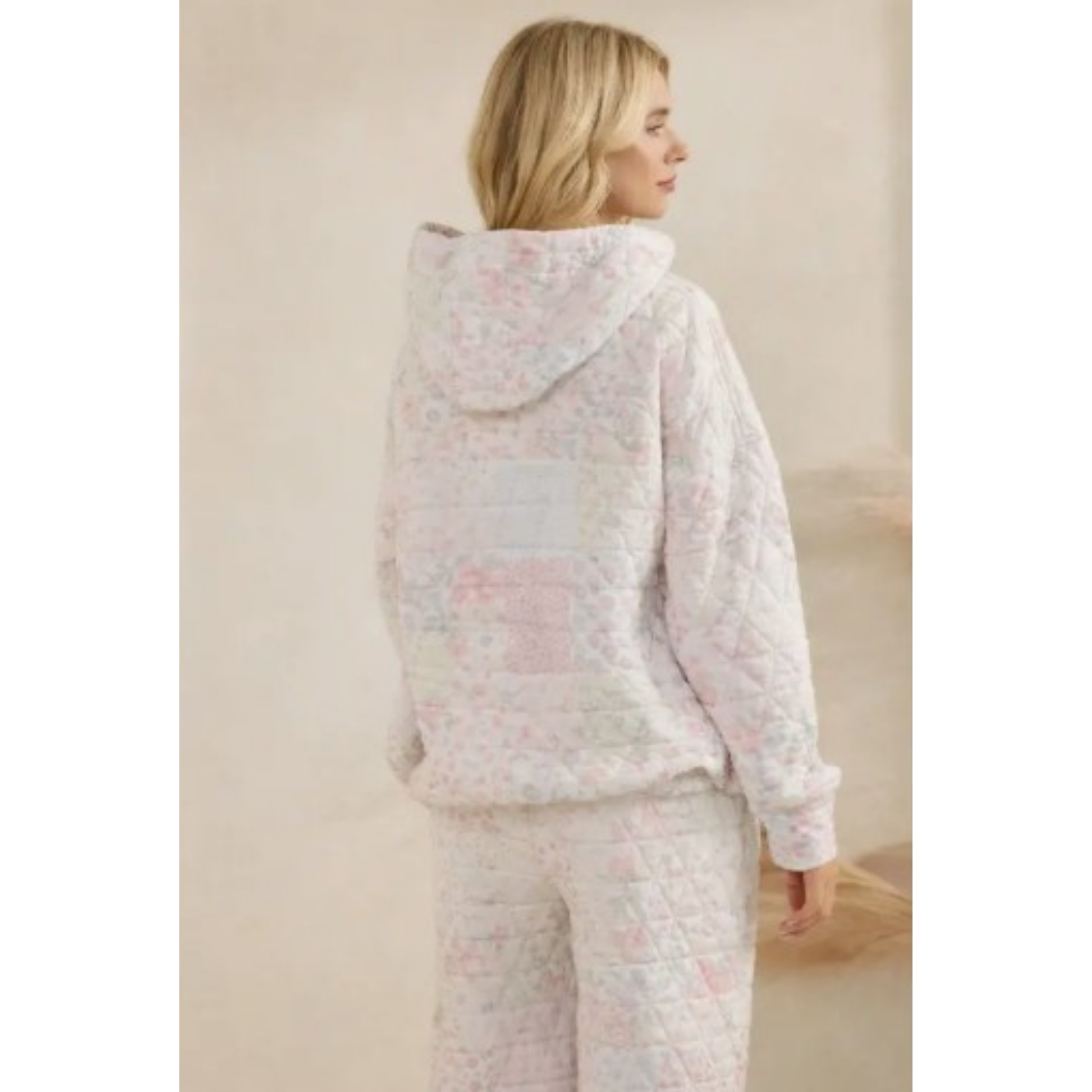 Woman wearing a pastel floral quilted hoodie set against a beige background