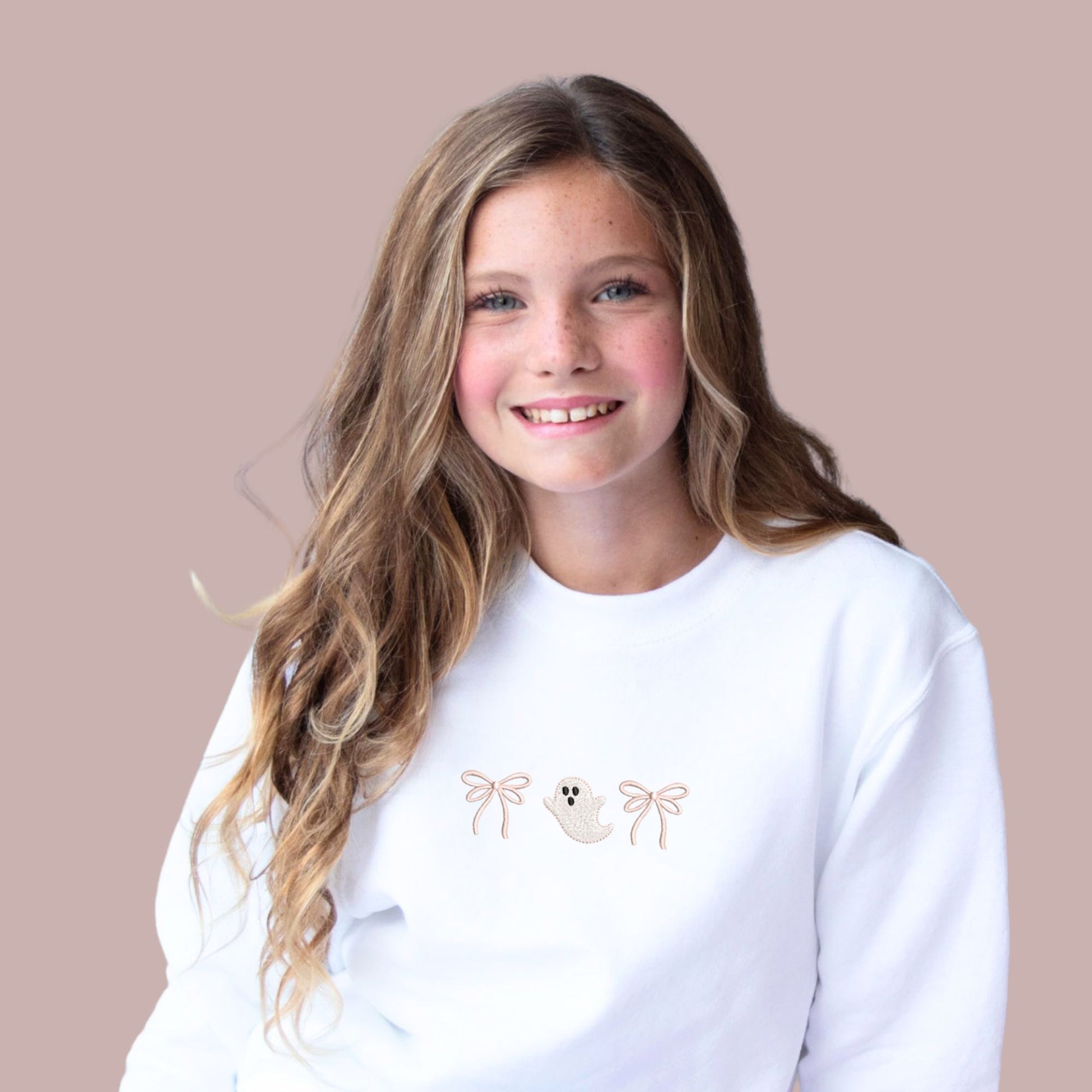 Little girl wearing a white sweatshirt with embroidered double loop pink bows and a cute ghost design