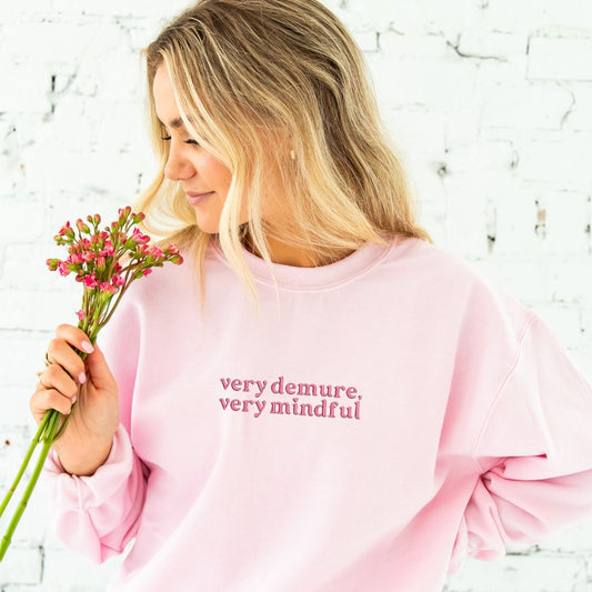 woman wearing a light pink crewneck with a pink very demure, very mindful embroidered design