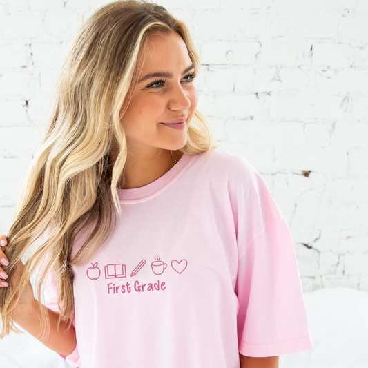 young woman wearing a blossom comfort colros t-shirt with embroidered teacher icons in pink thread across the chest and custom text underneith