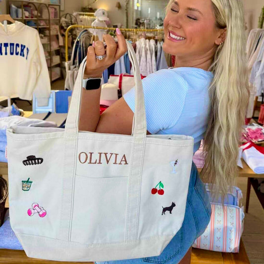 Woman holding a white tote bag with personalized designs and name in a store setting