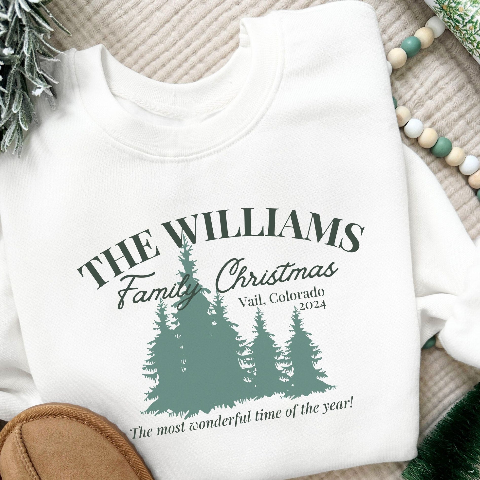 white youth sweatshirt with a custom christmas print featuring a family name, vacation location, year, trees, and a "The most wonderful time of the year!" quote in green ink