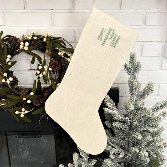 natural and silver striped stocking with custom name embroidered in font 16 and silver sage thread hanging at a fireplace