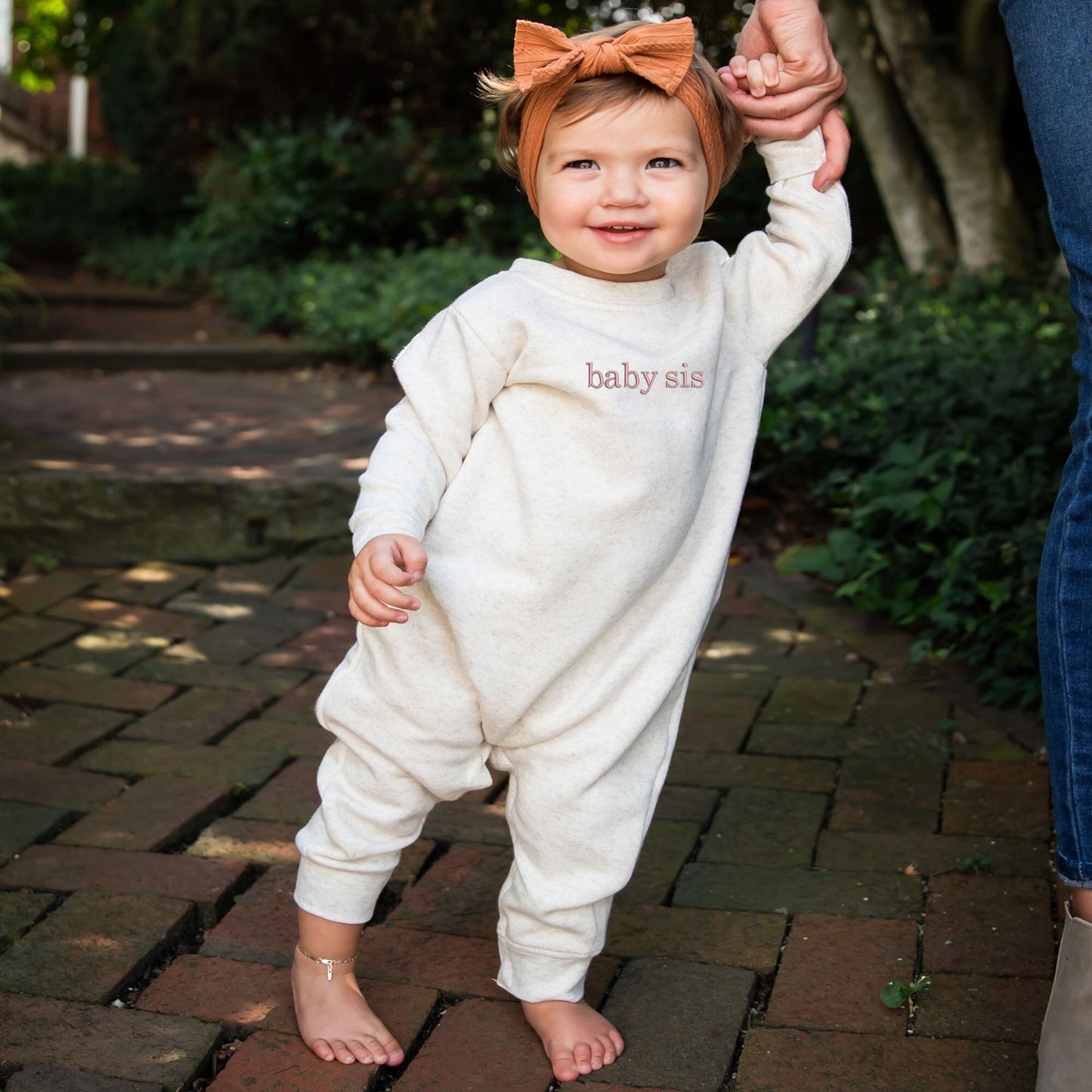 baby wearing a natural heather  fleece romper with embroidered baby sis in mauve thread on the chest