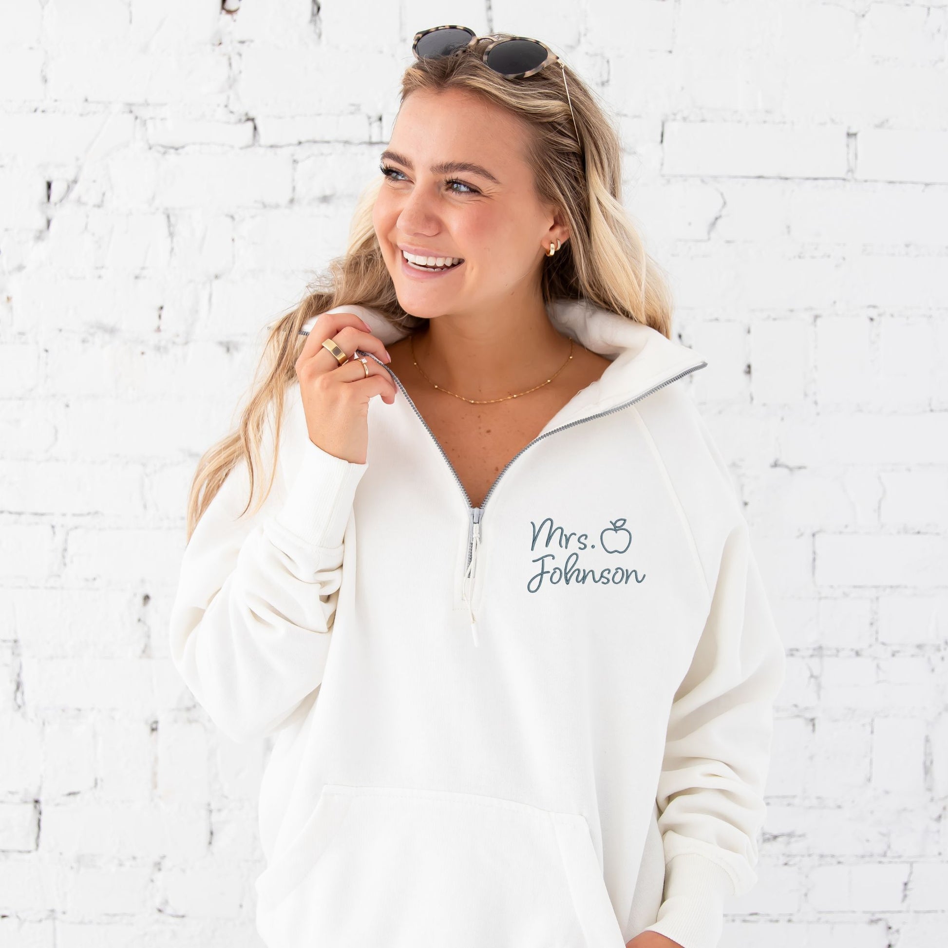 close up of woman wearing a white boxy ladies fit quarter zip pullover with a custom name and outlined apple embroidered in a french blue thread.