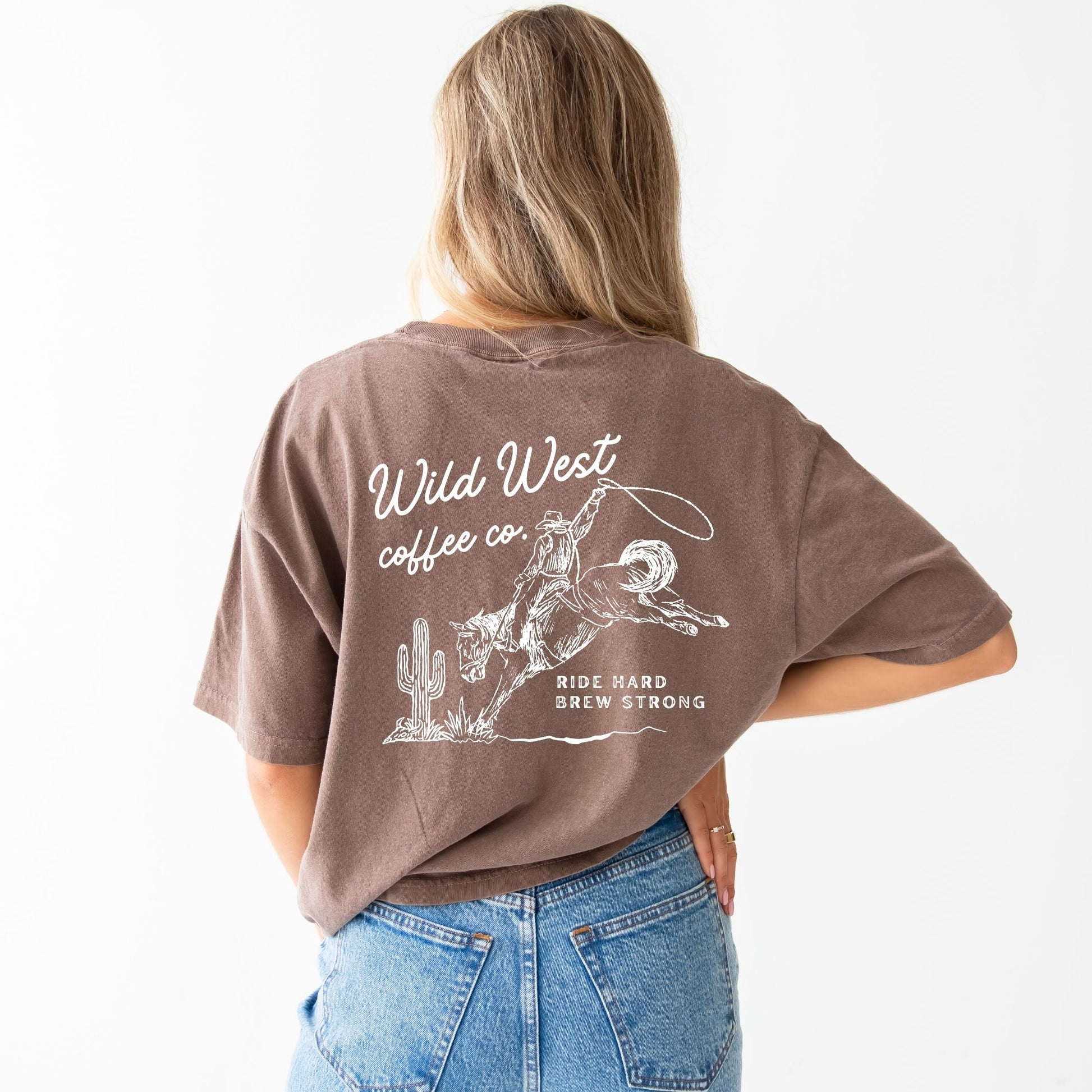 a woman wearing an espresso brown comfort colors t-shirt with a full cowboy western inspired print in white ink on the back