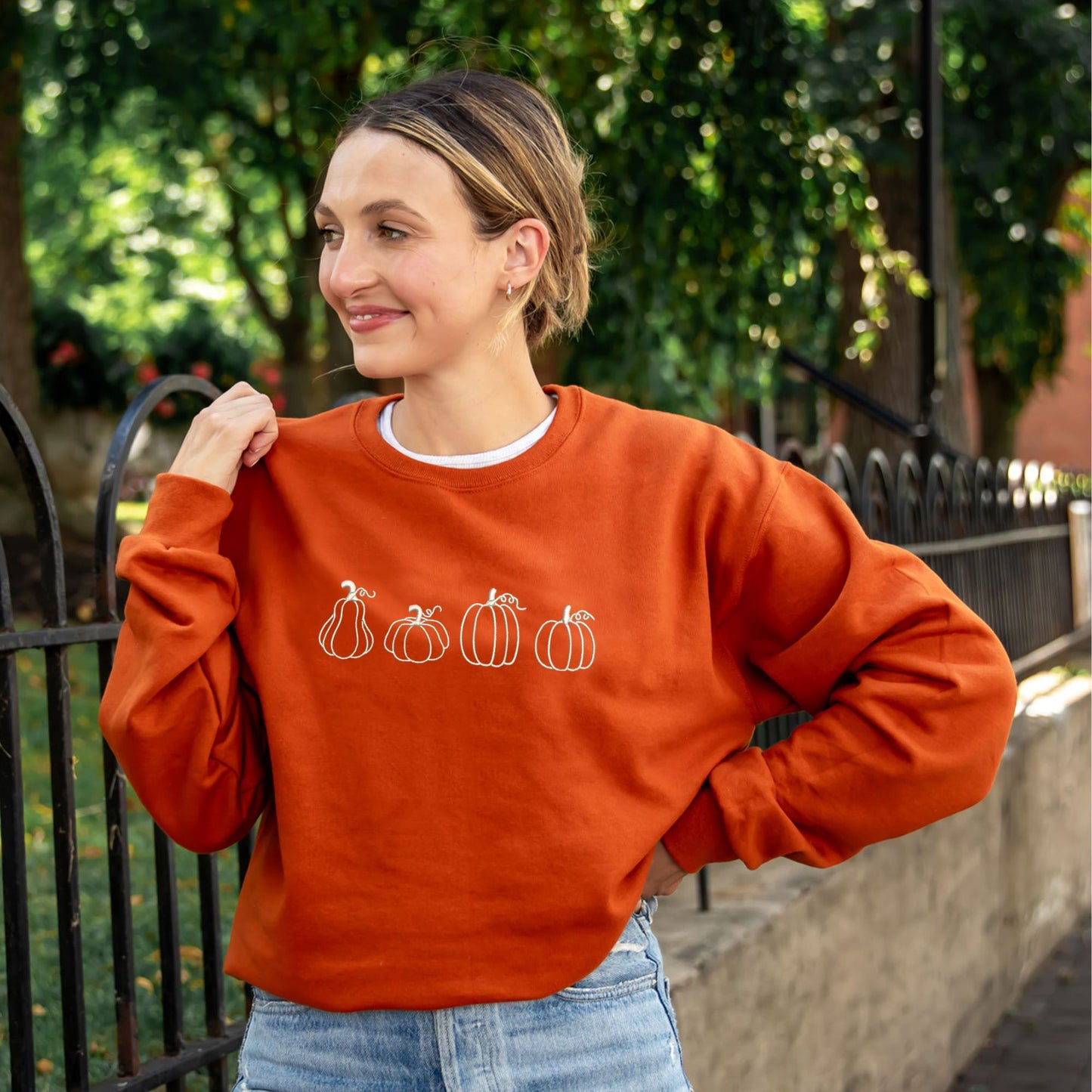 woman wearing a texas orange crewneck sweatshirt with 4 different pumpkin outlines embroidered across the chest in natural thread