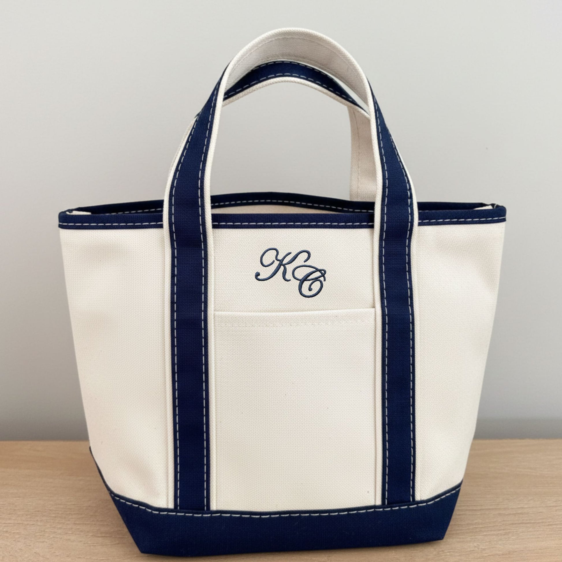 canvas tote bag with navy accents and an edwardian script monogram on a wooden surface.