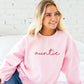 young woman wearing an oversized light pink crewneck sweatshirt with embroidered auntie in lowercase script font across the chest in pink thread