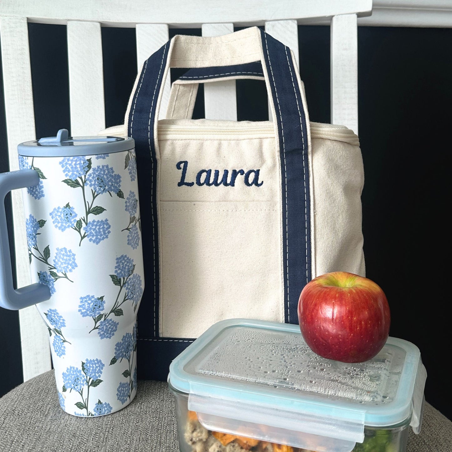 Tumbler with floral design, insulated lunch bag, and apple on a surface.