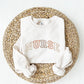 flat lay of a white crewneck sweatshirt with embroidered NURSE in all caps athletic block font curved across the chest in fall colors