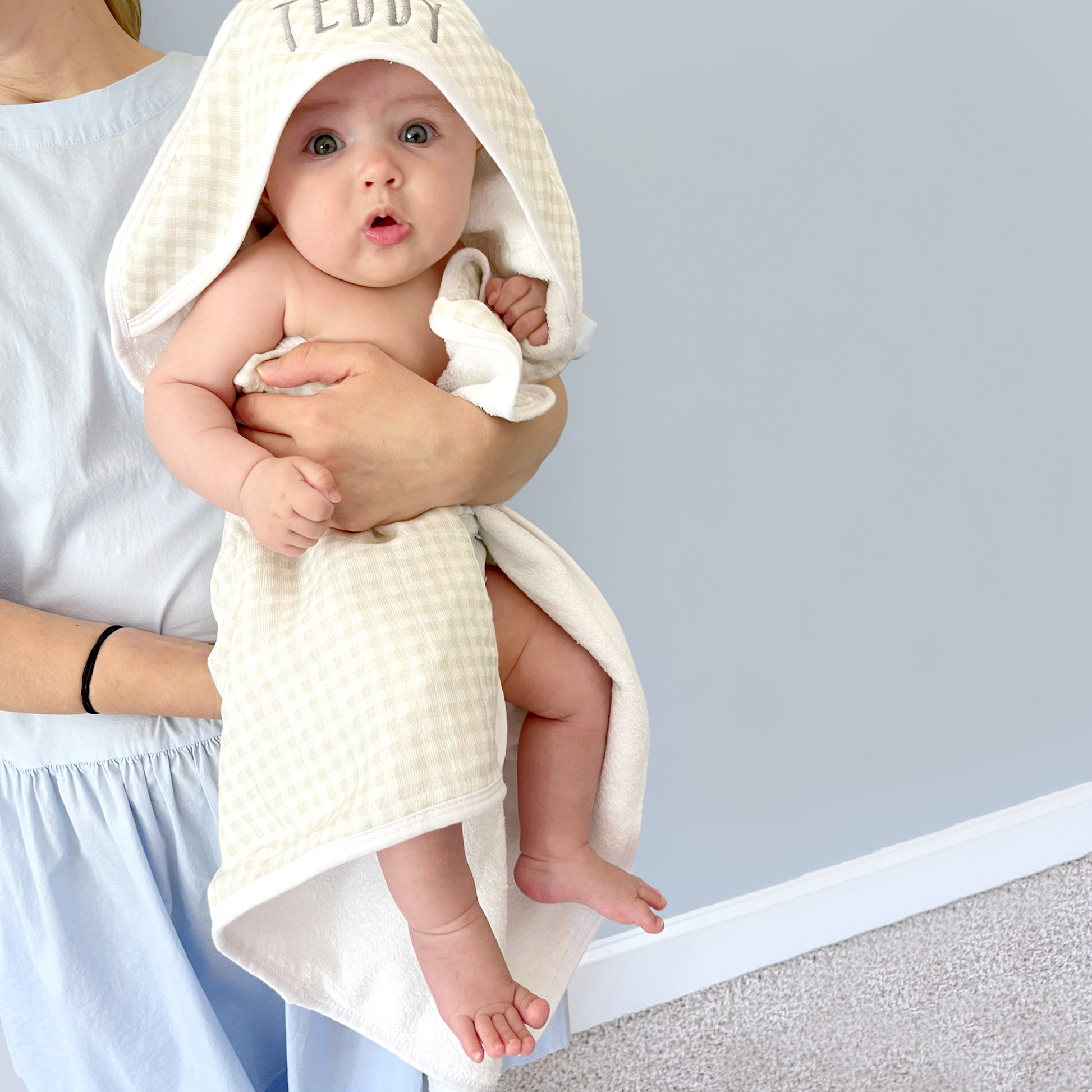 woman holding her baby wrapped in a tan plaid hooded bath towel with name embroidered on the hood in a dark gray thread