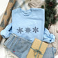 Christmas styled flat lay photo a light blue crewneck sweatshirt with3 embroidered snowflakes across the chest