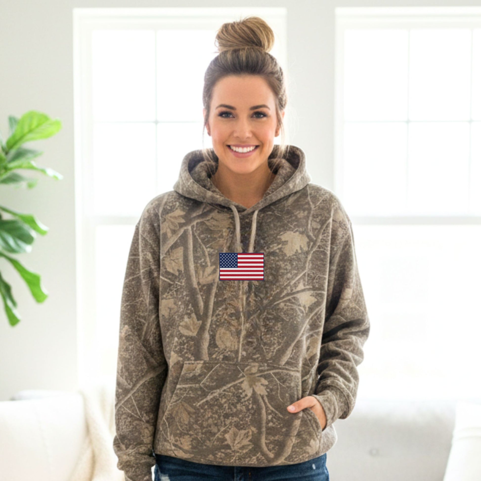 Woman wearing a camouflage hoodie with an American flag patch indoors.