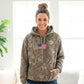 Woman wearing a camouflage hoodie with an American flag patch indoors.
