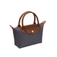 A small structured handbag in dark gray with brown leather handles, trim, and front flap, plus a gold-tone snap button, shown on a plain white background.