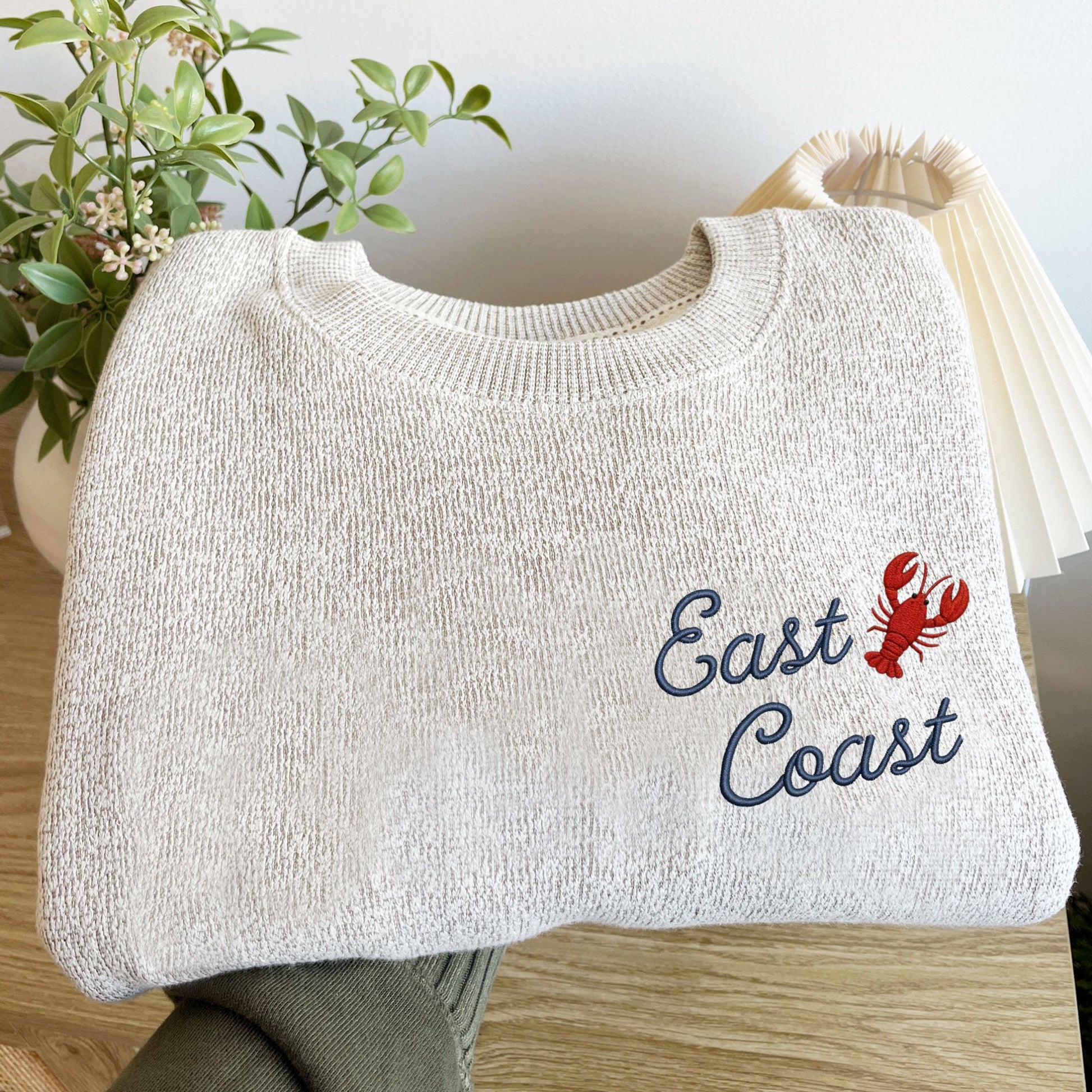 folded oatmeal heather cozy knit fleece crewneck sweatshirt with East Coast embroidered in a script font paired with a lobster on the left chest.