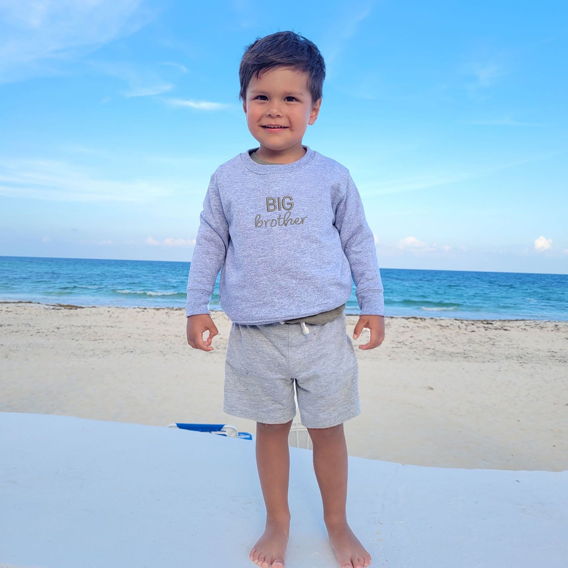 Little boy wearing heather crewneck with custom BIG brother embroidered design in gray thread