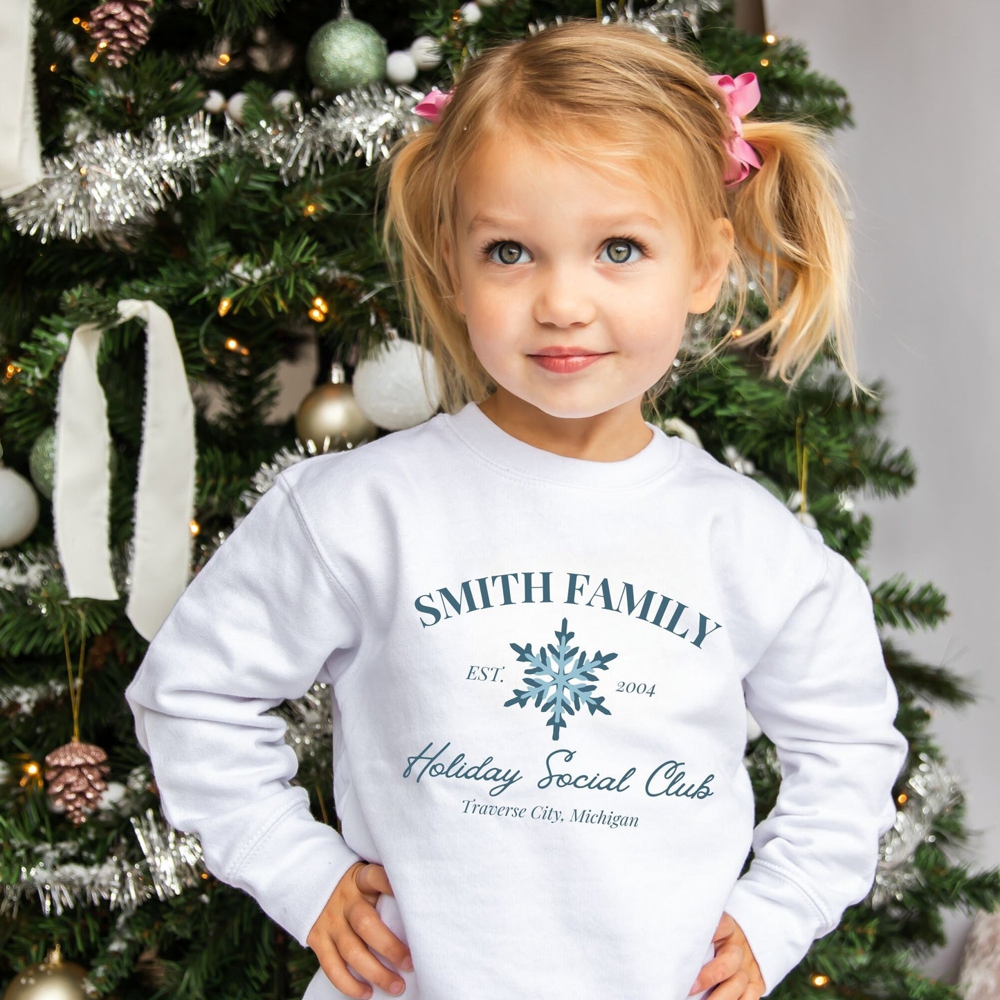 Little girl wearing a toddler crew with a custom print featuring a family name, Est date, snowflake, holiday social club, and location in blue