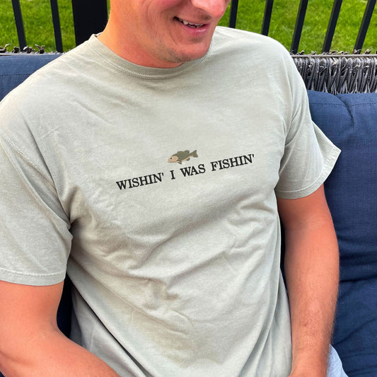 man wearing a bay comfort colors t-shirt with a custom embroidered design featuring a bass fist and "wishin' i was fishin'" on the center chest