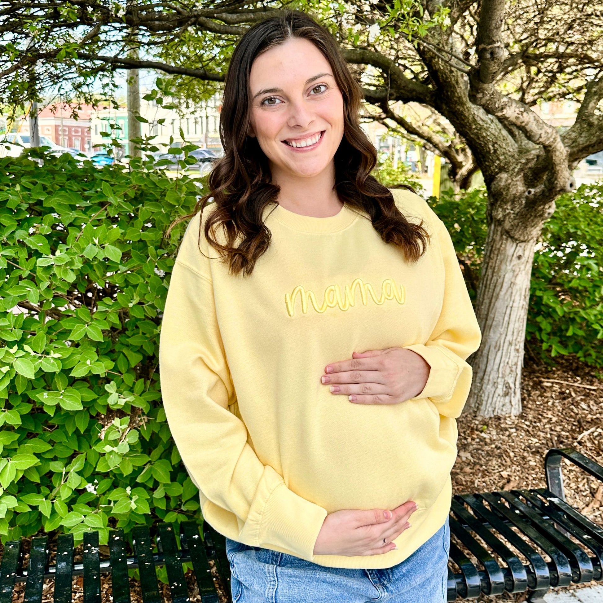 Woman wearing a yellow sweatshirt with 'MAMA' text, standing outdoors.