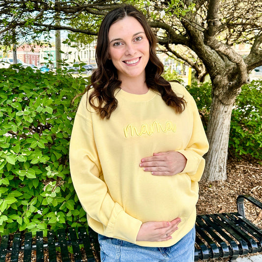 Woman wearing a yellow sweatshirt with 'MAMA' text, standing outdoors.