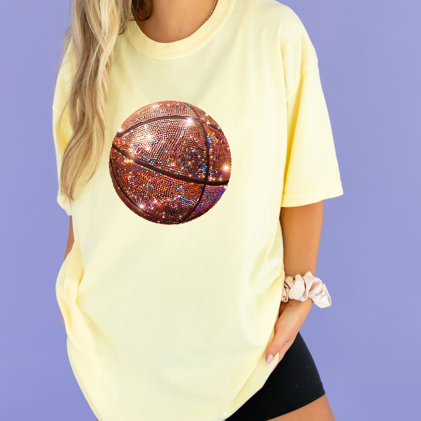 young woman wearing a banana comfort colors t-shirt with large glitter basketball print on the chest