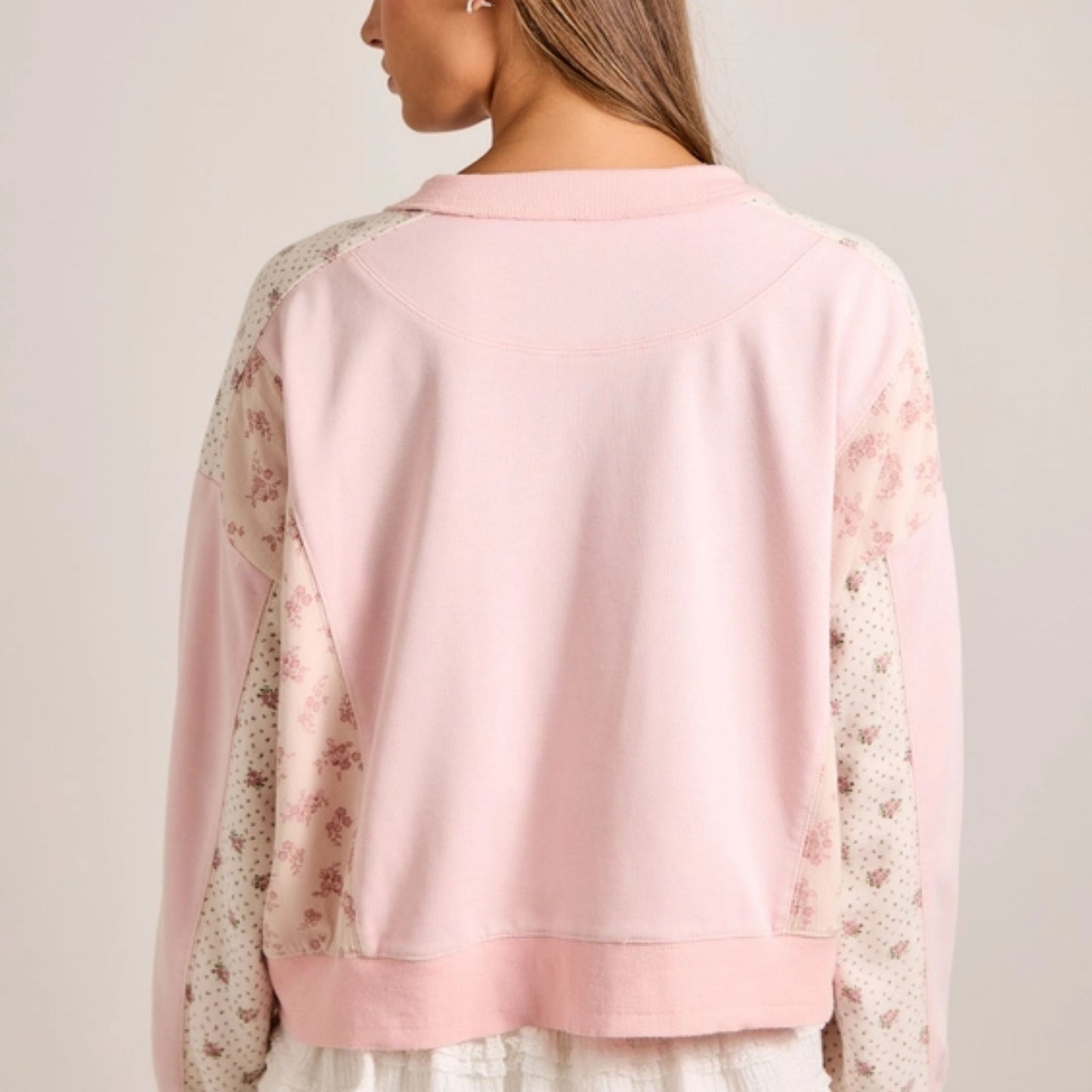 Pink crewneck with floral sleeves worn by a person on a plain background