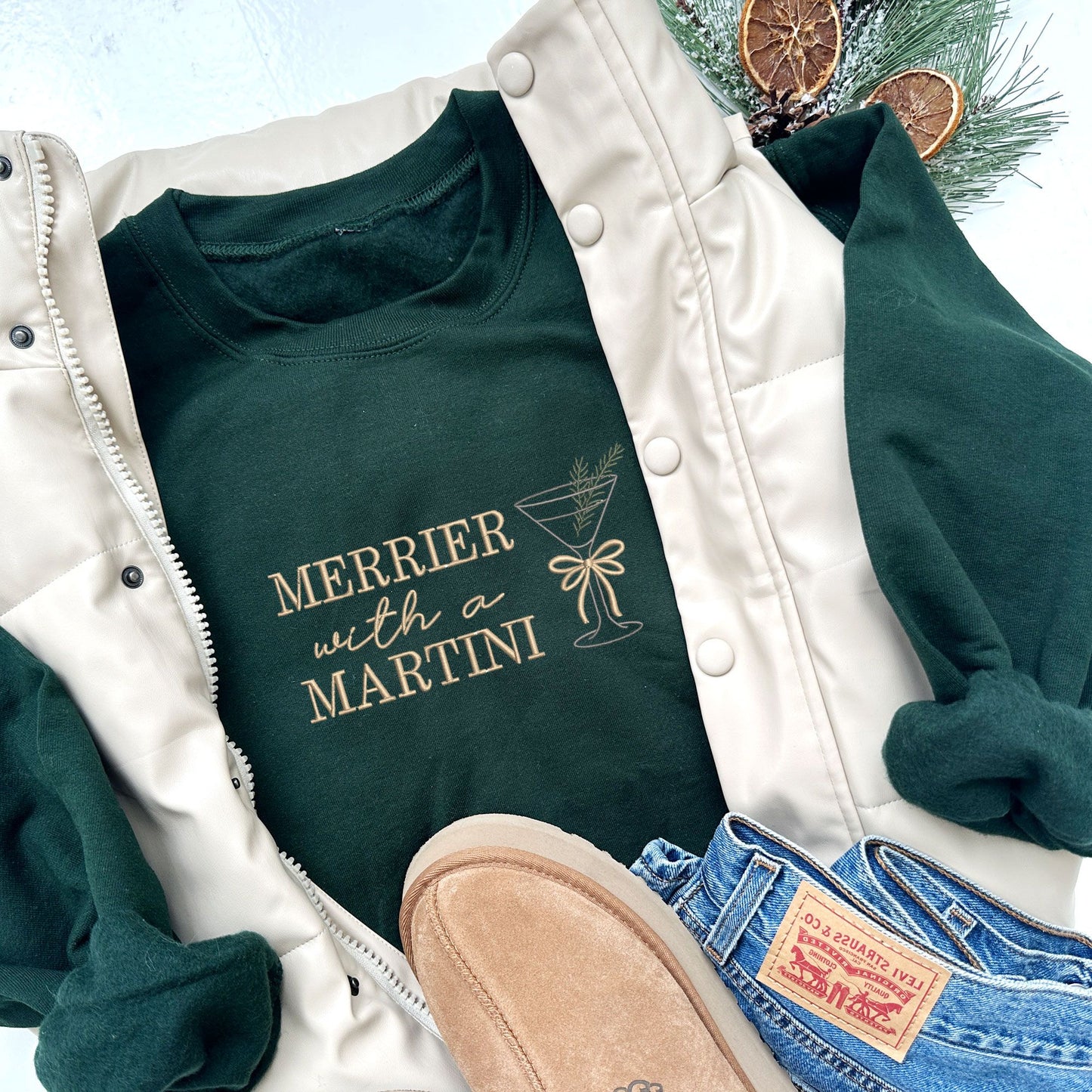 forest green crewneck sweatshirt with embroidered merrier with a martini text in camel thread and martini glass design with bow and pine sprig across the chest