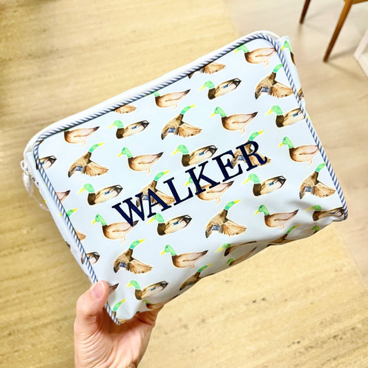 Rectangular zipper pouch with duck pattern and 'WALKER' text held by a hand on a wooden surface.