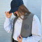 young woman wearing a lightweight grey fleece vest with a navy blue embroidered monogram on the left chest