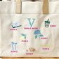 Beige tote bag with embroidered icons and text on a wooden surface