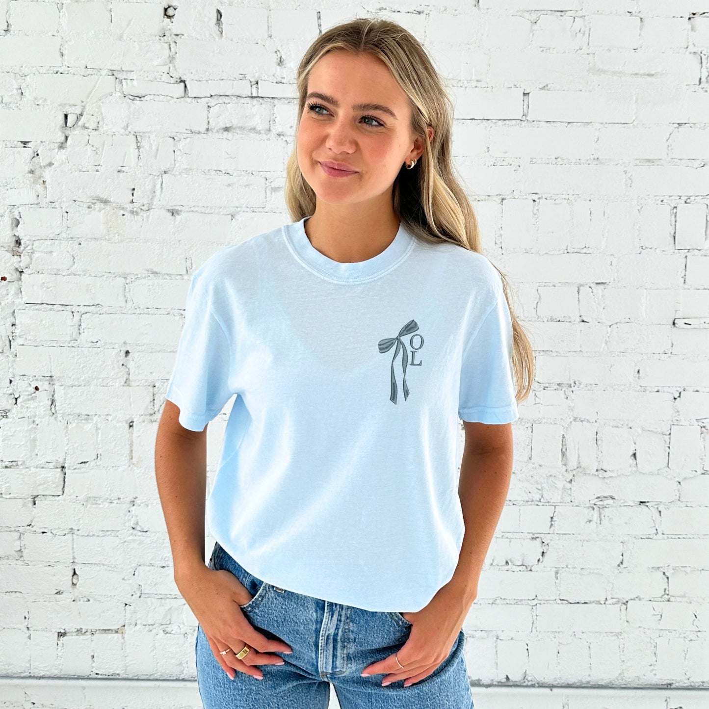 girl wearing a chambray comfort colors t-shirt with custom ribbon bow stacked initial embroidered design on the left chest in french blue thread.