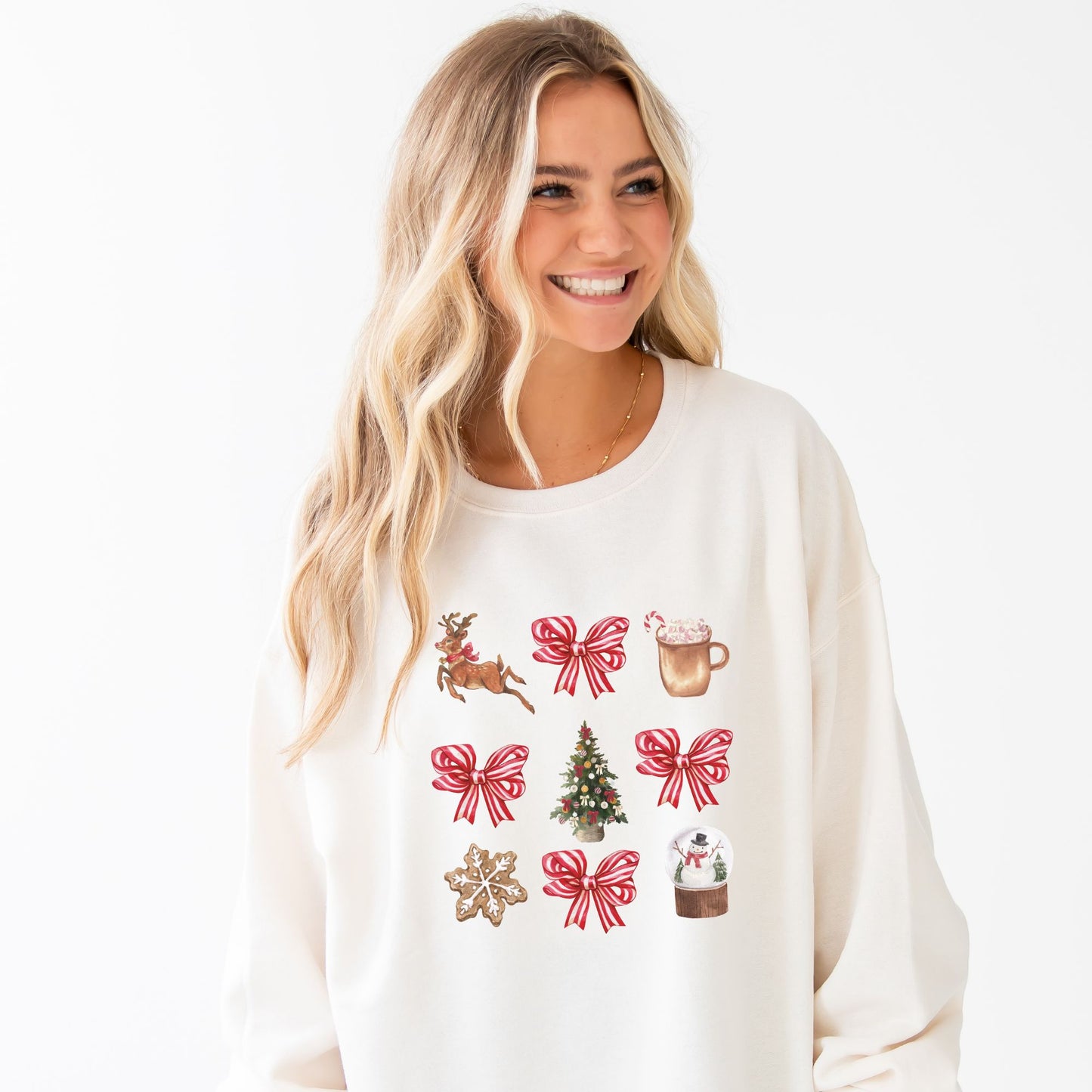 woman wearing a sweet cream pullover with a retro reindeer, bow, cocoa, tree, cookie, and snow globe printed design