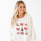 woman wearing a sweet cream pullover with a retro reindeer, bow, cocoa, tree, cookie, and snow globe printed design