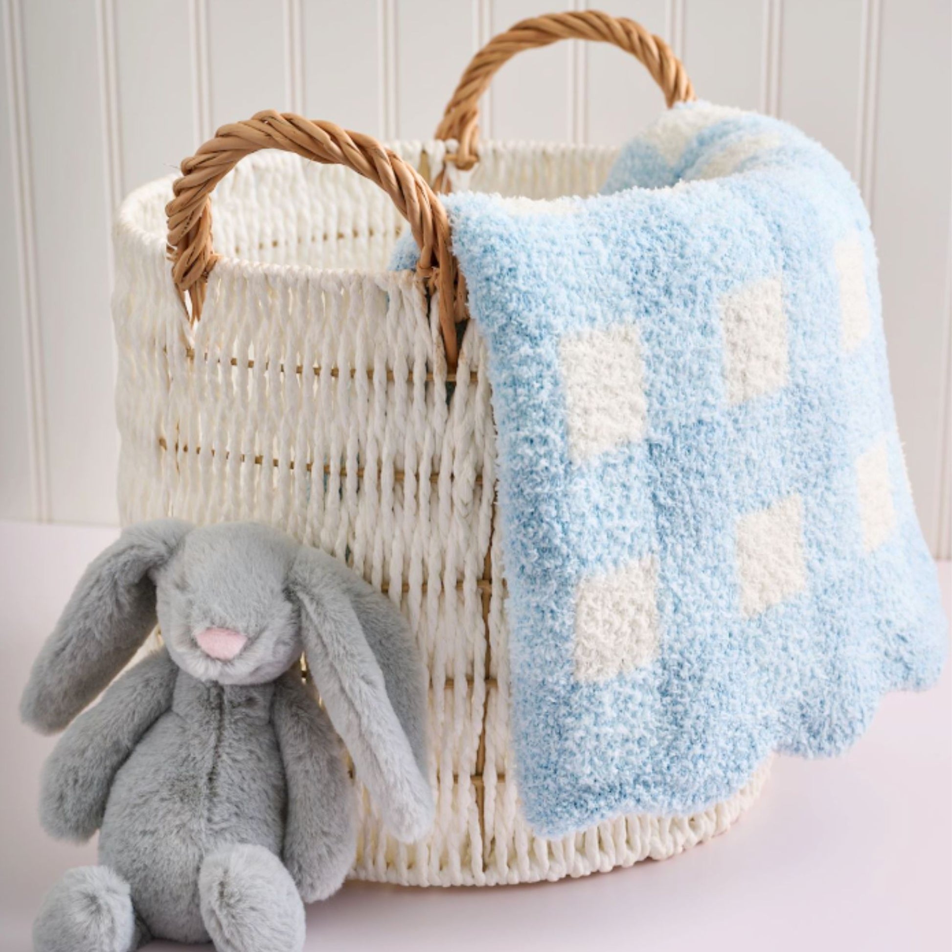 Wicker basket with blue and white checkered blanket and gray plush bunny toy on a light background