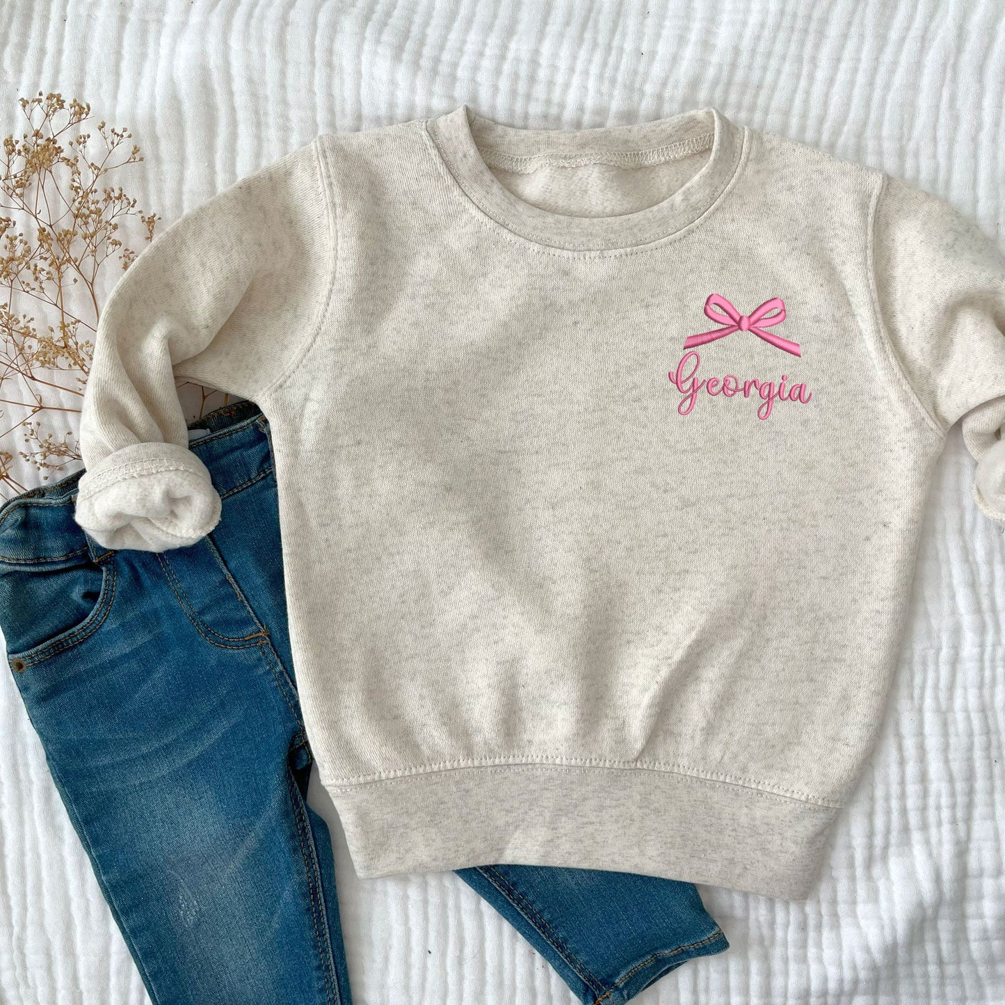 natural heather toddler crewneck with embroidered name and bow on the left chest in pink  thread.