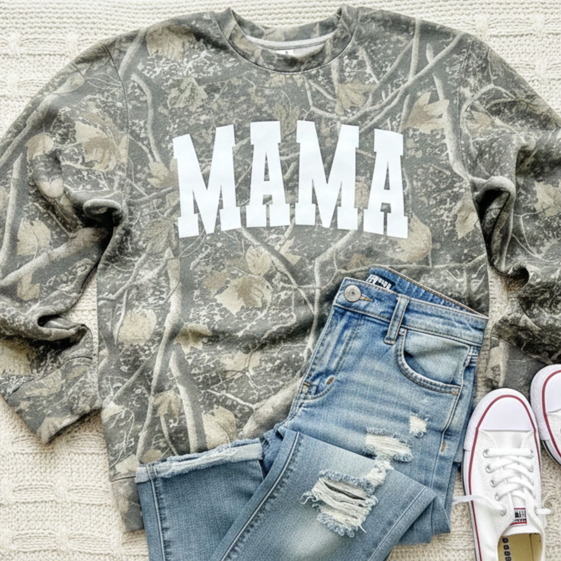 Camouflage sweatshirt with 'MAMA' text, blue jeans, and white sneakers on a light background