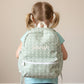 Child wearing a sage green floral patterned backpack with 'Sarah' embroidered on it against a beige background