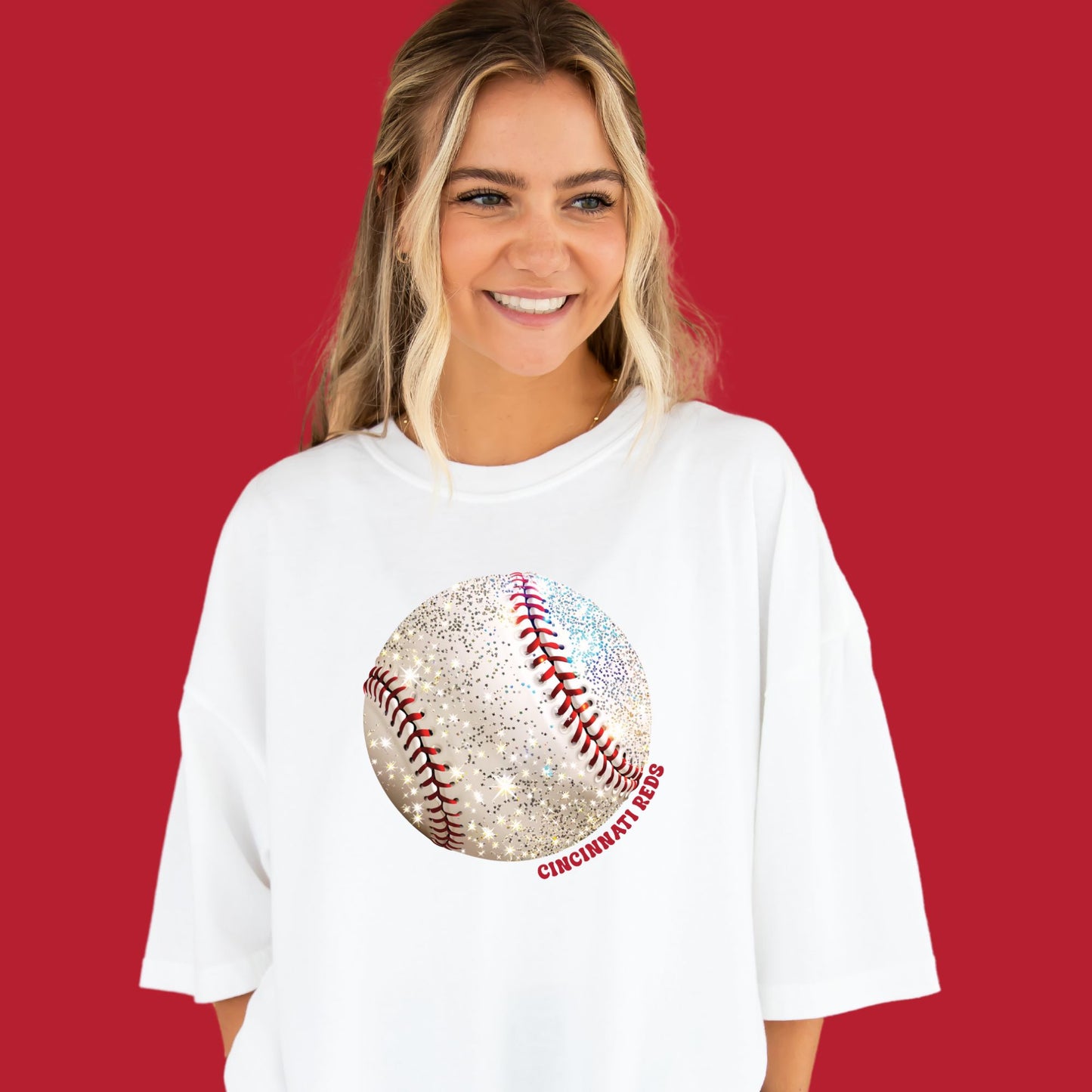 young woman wearing a white comfort colors t-shirt with large glitter baseball print and Cincinnati Reds text curved around the design in red ink