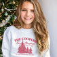 young girl wearing a white youth sweatshirt with a custom christmas print featuring a family name, vacation location, year, trees, and a "The most wonderful time of the year!" quote in red ink