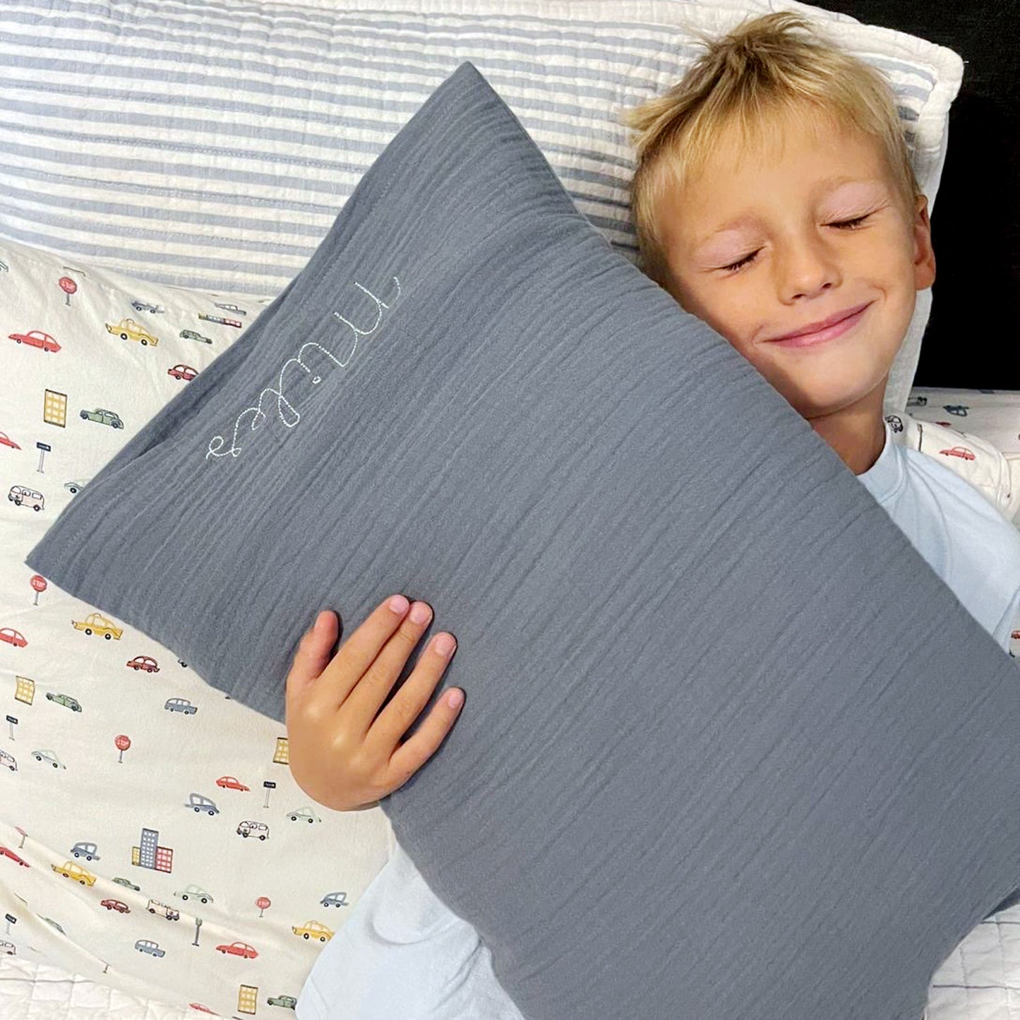 little boy hugging on a custom pillow with a muslin pillowcase and personalized name stitched embroidery along the side