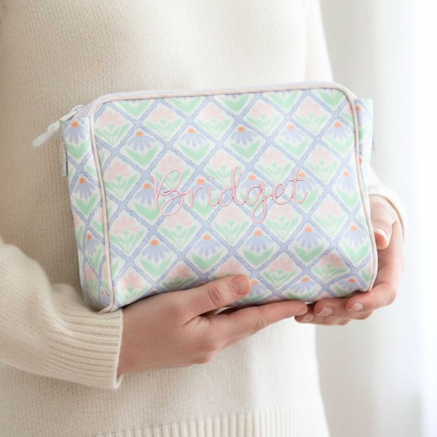 Person holding a pastel patterned pouch with 'Bridget' embroidered on it.
