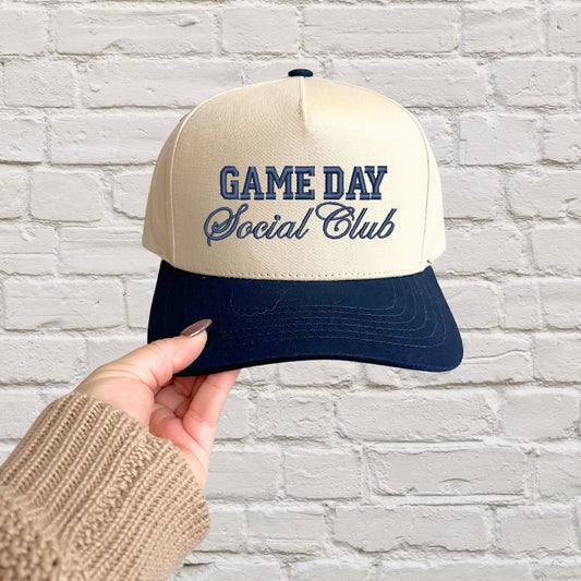 two toned navy canvas trucker hat with a game day social club embroidered design in navy thread.