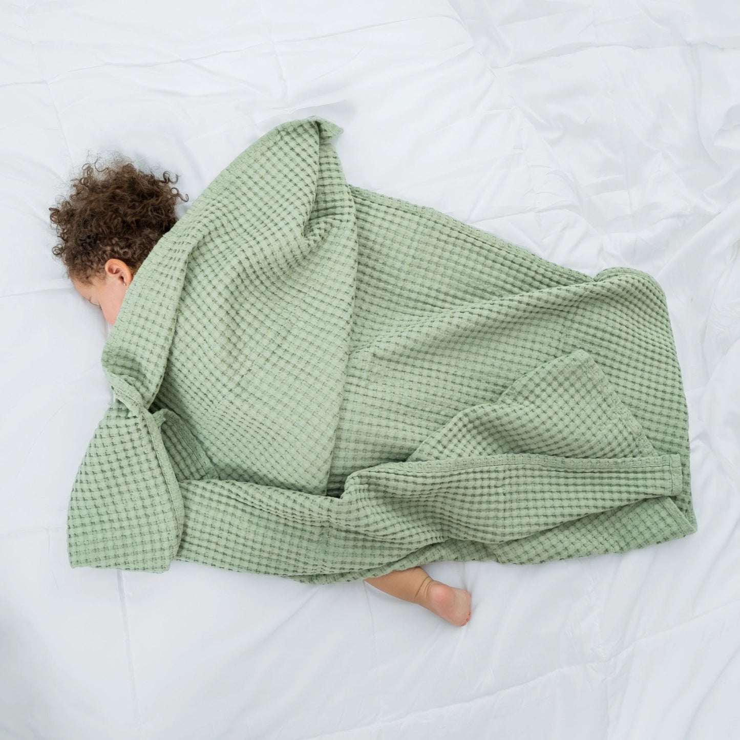 baby laying down covered by sage green waffle weave blanket