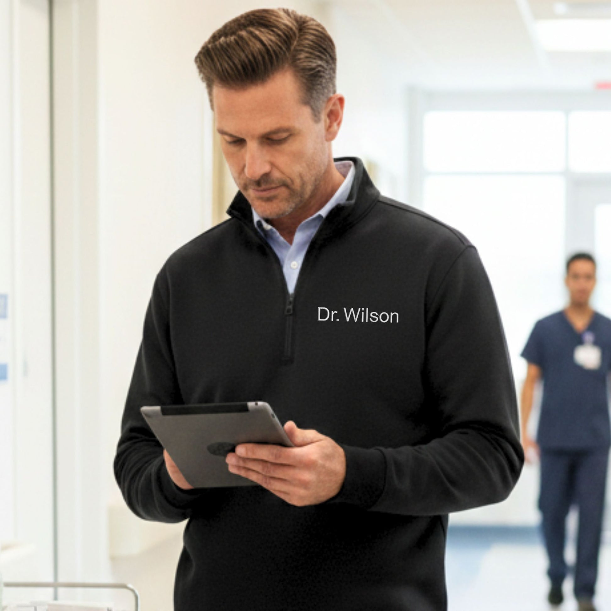 Man in a black jacket with 'Dr. Wilson' on it, holding a tablet in a hospital setting.