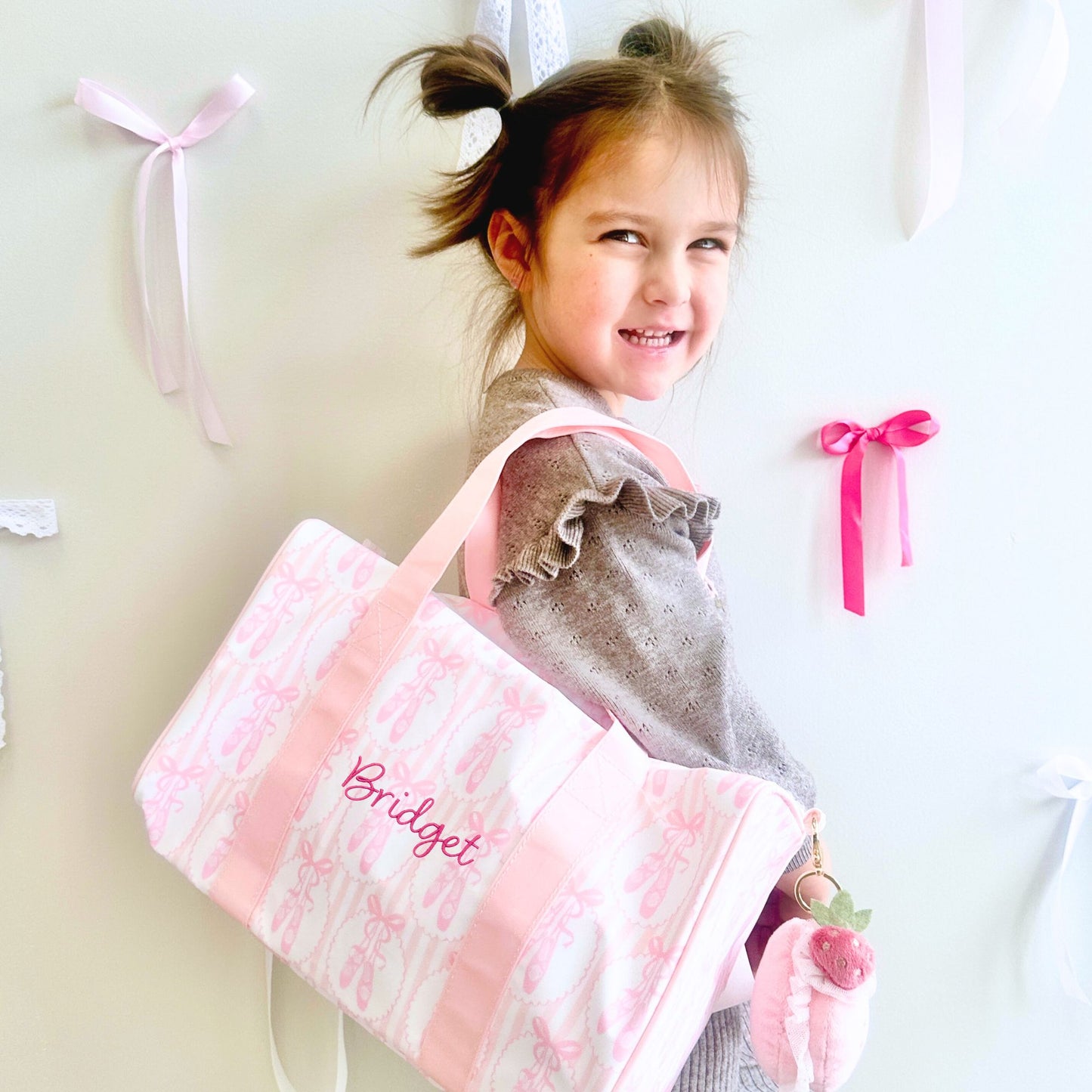 Young girl holding a pink bag with 'Bridget' embroidered on it, against a light background.